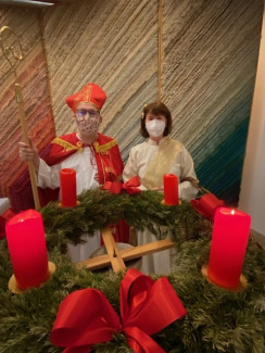 Pastref. Mauser und Pfrin. Eunicke im Kostüm vor einem Adventskranz